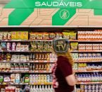 Prateleiras de supermercado com suplementos alimentares e produtos saudáveis, enquanto consumidora passa pelo corredor.
